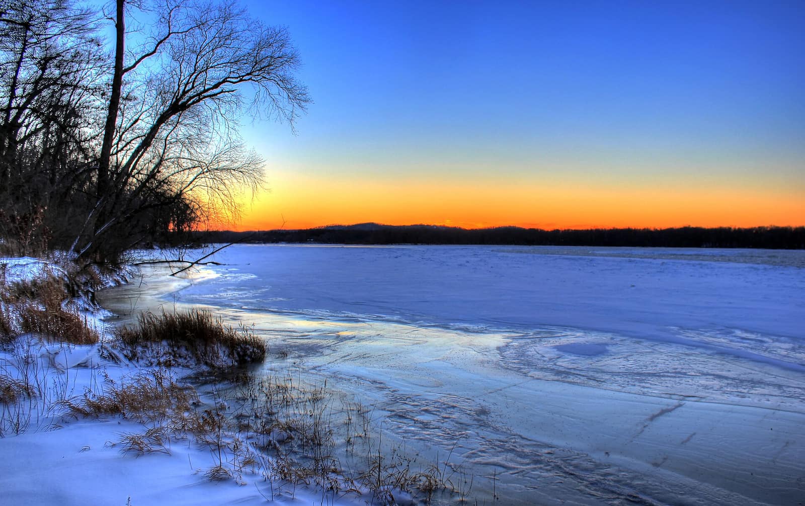 Frozen Wisconsin River at sunset in winter near the Dells, with snow-covered banks and a vivid orange-blue sky
